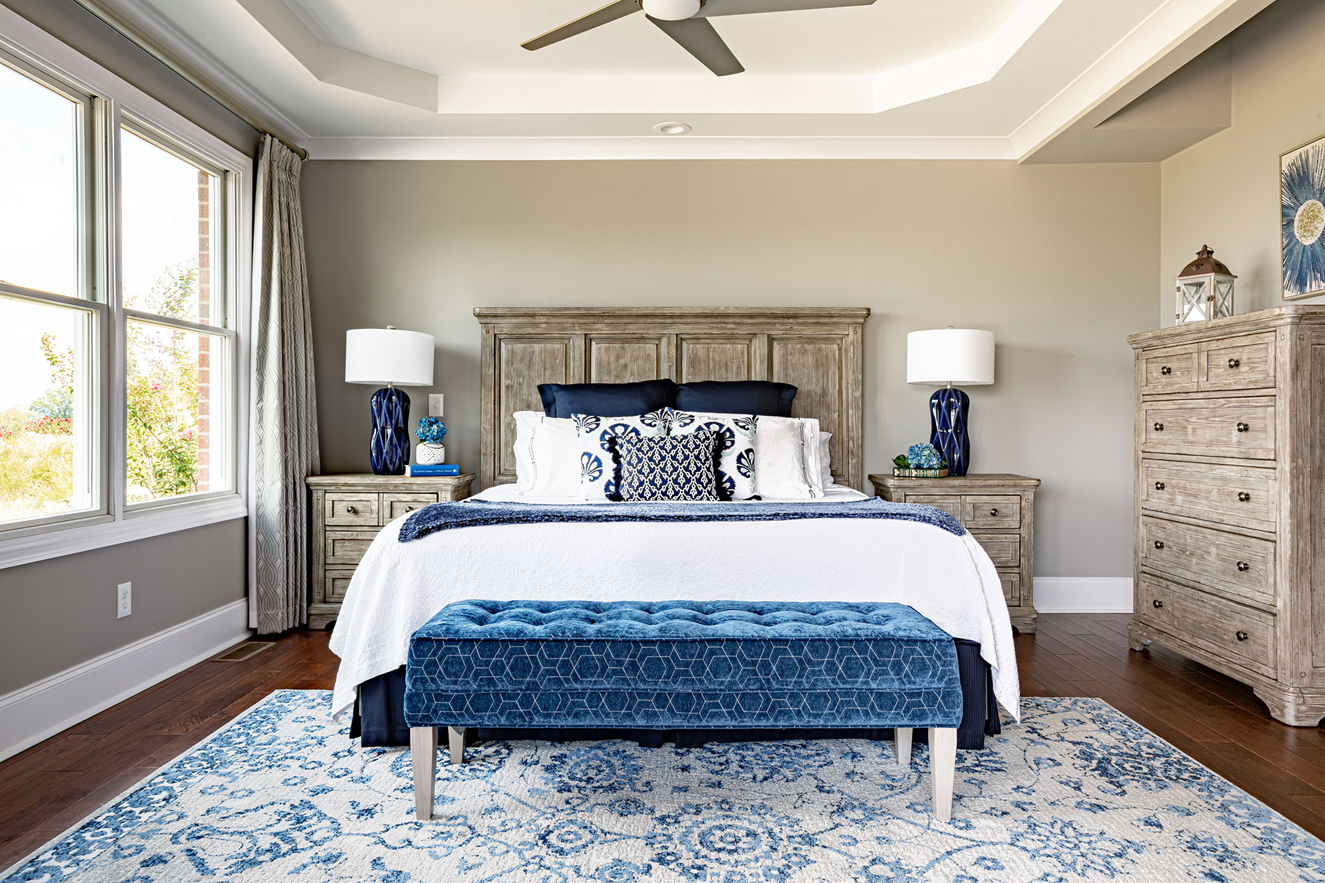 A photo of a serene and elegant bedroom with a white and blue upholstered bed, two nightstands, a dresser, and a cozy sitting area.