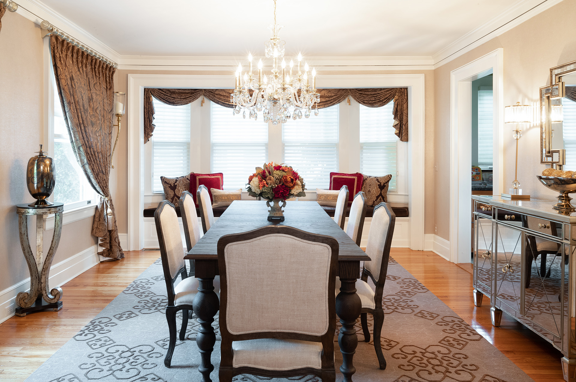 A photo of a modern dining room with a rectangular table, six chairs, a chandelier, and a large mirror on the wall.